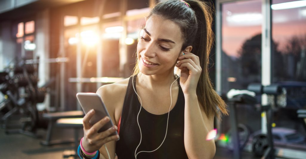Happy woman putting on headphone in the gym - Simply Gym
